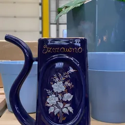 Close-up van een donkerblauwe keramische kan met bloemmotief en gouden decoratie
