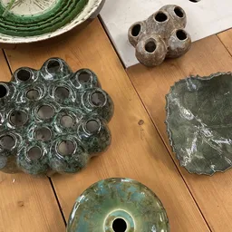 Diverse bronzen archeologische voorwerpen op houten tafel, waaronder decoratieve schalen met gaten en vaasjes