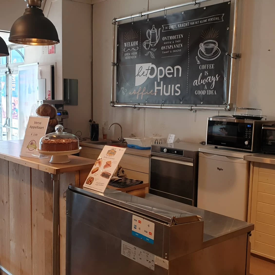 Keukenhoek met apparaten, houten werkblad en bord met 'Open Huis' en koffie-gerelateerde teksten