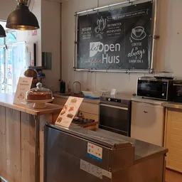 Keukenhoek met apparaten, houten werkblad en bord met 'Open Huis' en koffie-gerelateerde teksten