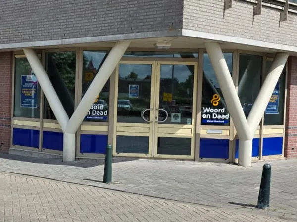 Gevel van kringloopwinkel met blauwe onderpui, glazen deuren en grote witte steunpilaren
