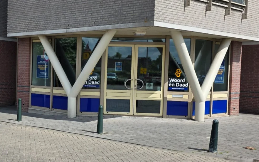Gevel van kringloopwinkel met blauwe onderpui, glazen deuren en grote witte steunpilaren