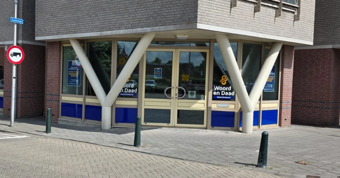 Gevel van kringloopwinkel met blauwe onderpui, glazen deuren en grote witte steunpilaren