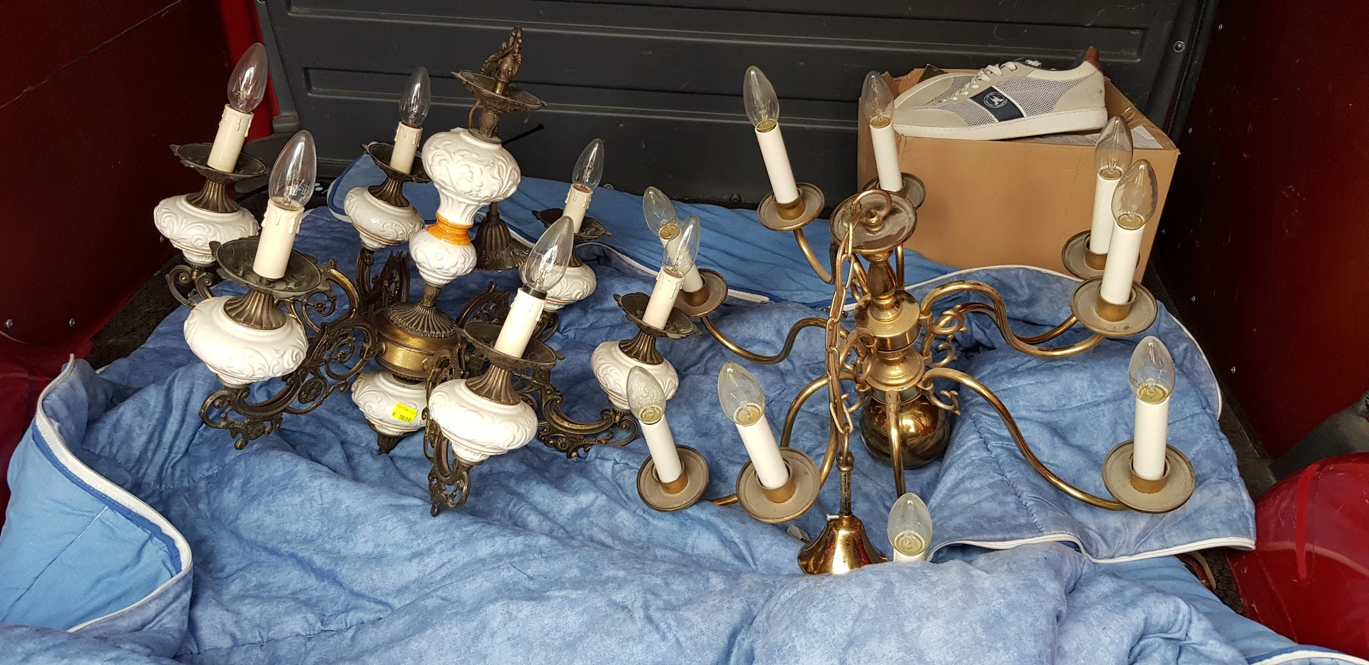 Verzameling gouden en messing kandelaars en wandlampjes met witte kaarsen op blauwe doek