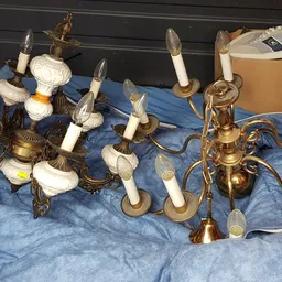Verzameling gouden en messing kandelaars en wandlampjes met witte kaarsen op blauwe doek