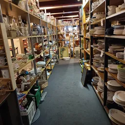 Winkelgang met houten stellingen vol serviesgoed, borden en huishoudartikelen aan beide zijden