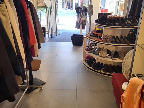 Winkelinterieur met kledingrekken links en schoenenrekken rechts, duidelijk zicht op winkelvloer en ingang