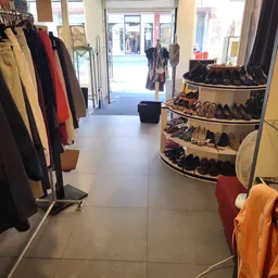 Winkelinterieur met kledingrekken links en schoenenrekken rechts, duidelijk zicht op winkelvloer en ingang