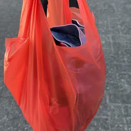 Rode plastic boodschappentas met donkerblauwe binnenzijde en een gat in de stof
