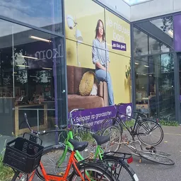 Gevel van kringloopwinkel met gele en paarse banden, grote raamuitstalling, fietsen met groene frame ervoor geparkeerd