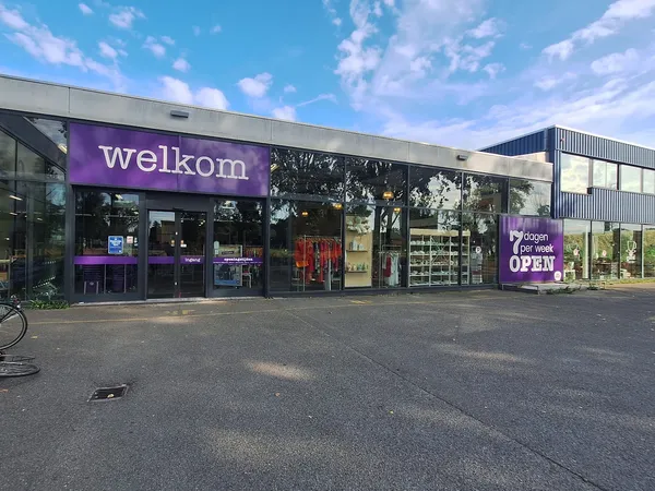 Gevel van kringloopwinkel Welkom met paarse branding, glazen ingang en etalages aan Eerste Stationsstraat
