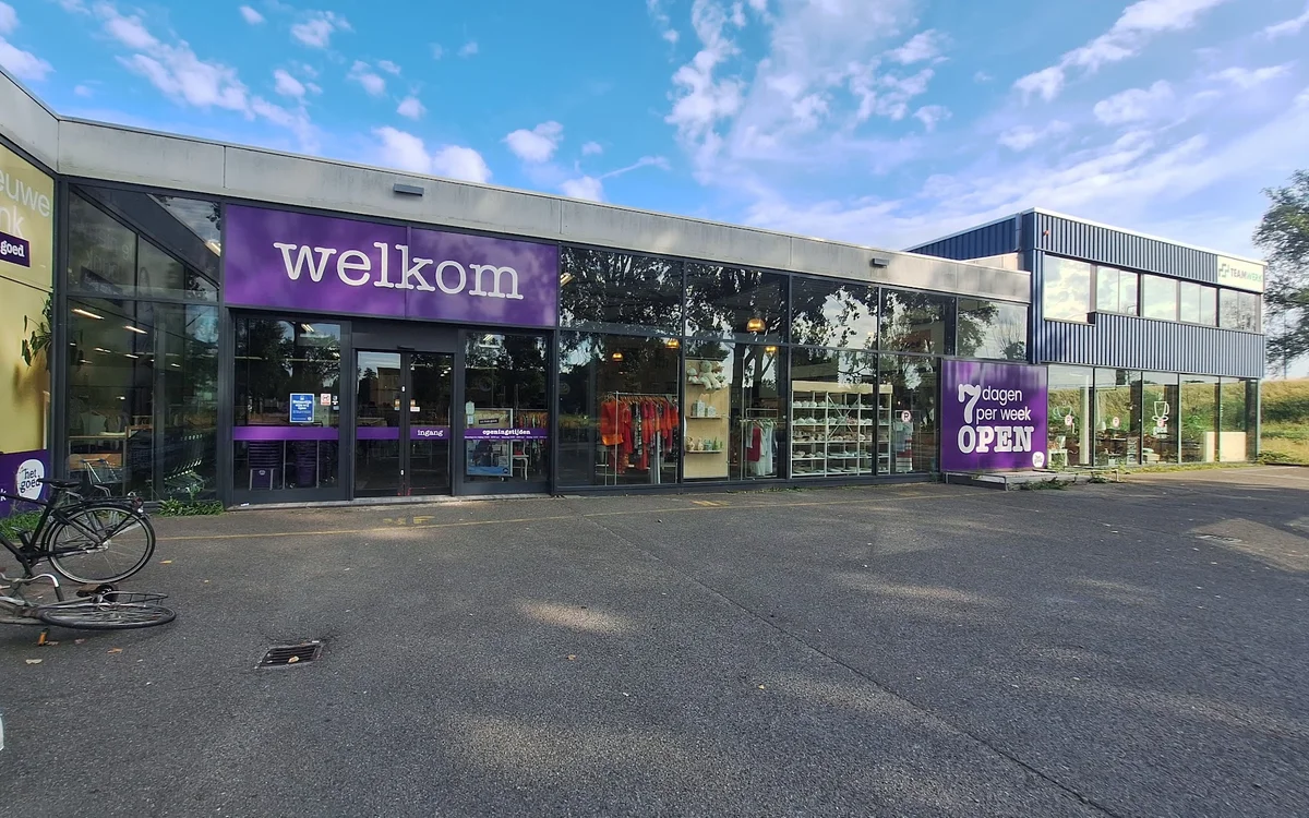 Gevel van kringloopwinkel Welkom met paarse branding, glazen ingang en etalages aan Eerste Stationsstraat
