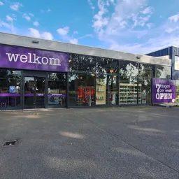 Gevel van kringloopwinkel Welkom met paarse branding, glazen ingang en etalages aan Eerste Stationsstraat