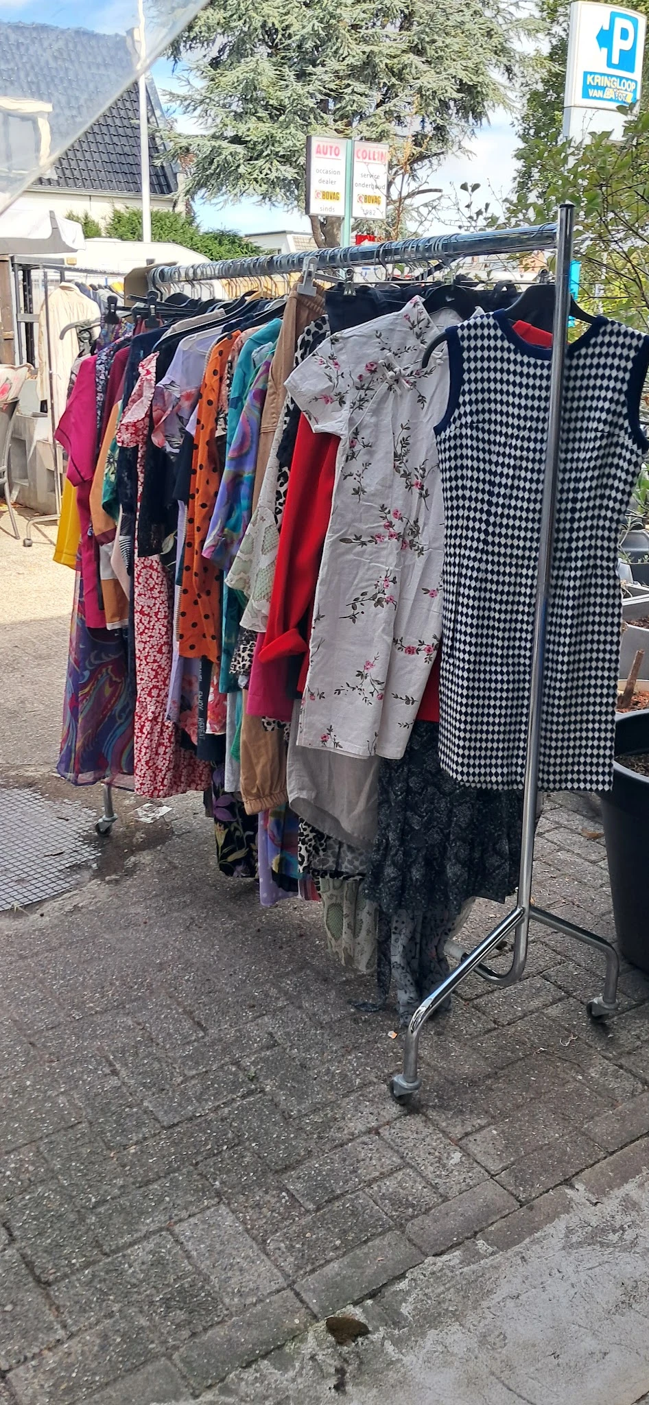 Rekken met tweedehands dameskleding in verschillende kleuren en patronen, waaronder rode, blauwe en zwart-witte items