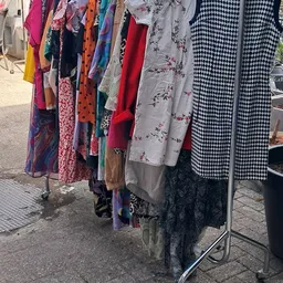 Rekken met tweedehands dameskleding in verschillende kleuren en patronen, waaronder rode, blauwe en zwart-witte items