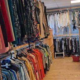 Rekken met tweedehands kleding in verschillende kleuren en stijlen in een kringloopwinkel