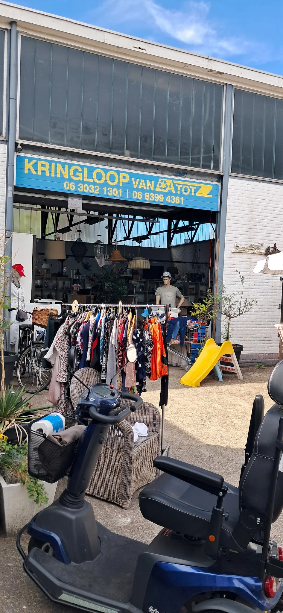 Rekken met tweedehands kleding en accessoires buiten voor de winkel uitgestald