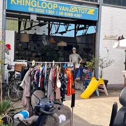 Rekken met tweedehands kleding en accessoires buiten voor de winkel uitgestald