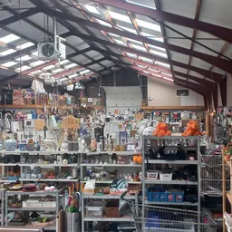 Overzicht van de winkelruimte met stellingen vol huishoudartikelen, decoratie en tweedehands spullen onder een industrieel pl
