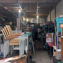 Winkelvloer met gestapelde stoelen, stellingen met diverse artikelen en veel spullen in een kringloopwinkel