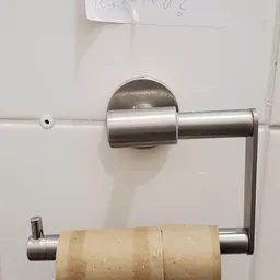 Close-up van een roestvrijstalen toiletpapierdispenser aan een witte wand