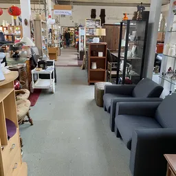 Winkelvloer van kringloopwinkel met meubels, stellingen en diverse artikelen langs het pad