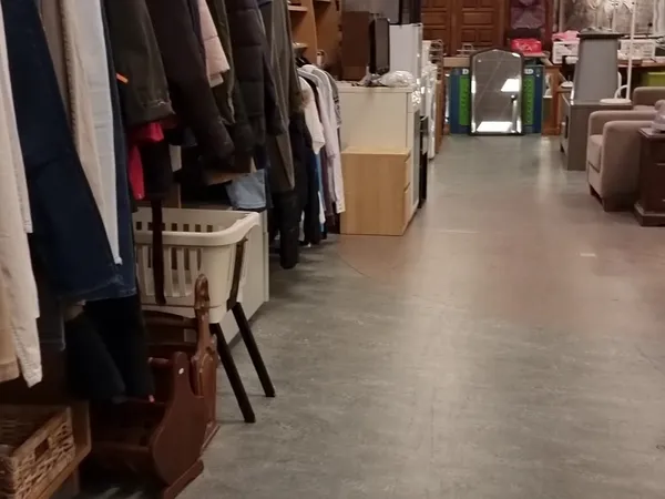 Overzicht van kringloopwinkel met kledingrekken, dozen en meubilair langs de wanden