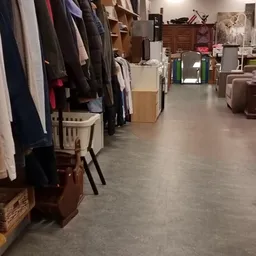 Overzicht van kringloopwinkel met kledingrekken, dozen en meubilair langs de wanden