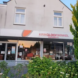Gevel van kringloopwinkel Kaatsheuvel met logo en grote ramen waarachter spullen zichtbaar zijn