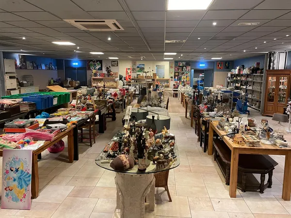 Overzicht van kringloopwinkelruimte met tafels vol diverse tweedehands artikelen, stellingen en kasten langs de muren