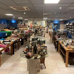Overzicht van kringloopwinkelruimte met tafels vol diverse tweedehands artikelen, stellingen en kasten langs de muren