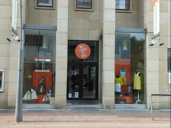 Winkelgevel met glazen deuren en ramen, oranje accenten in de vitrine en etalage met kleding