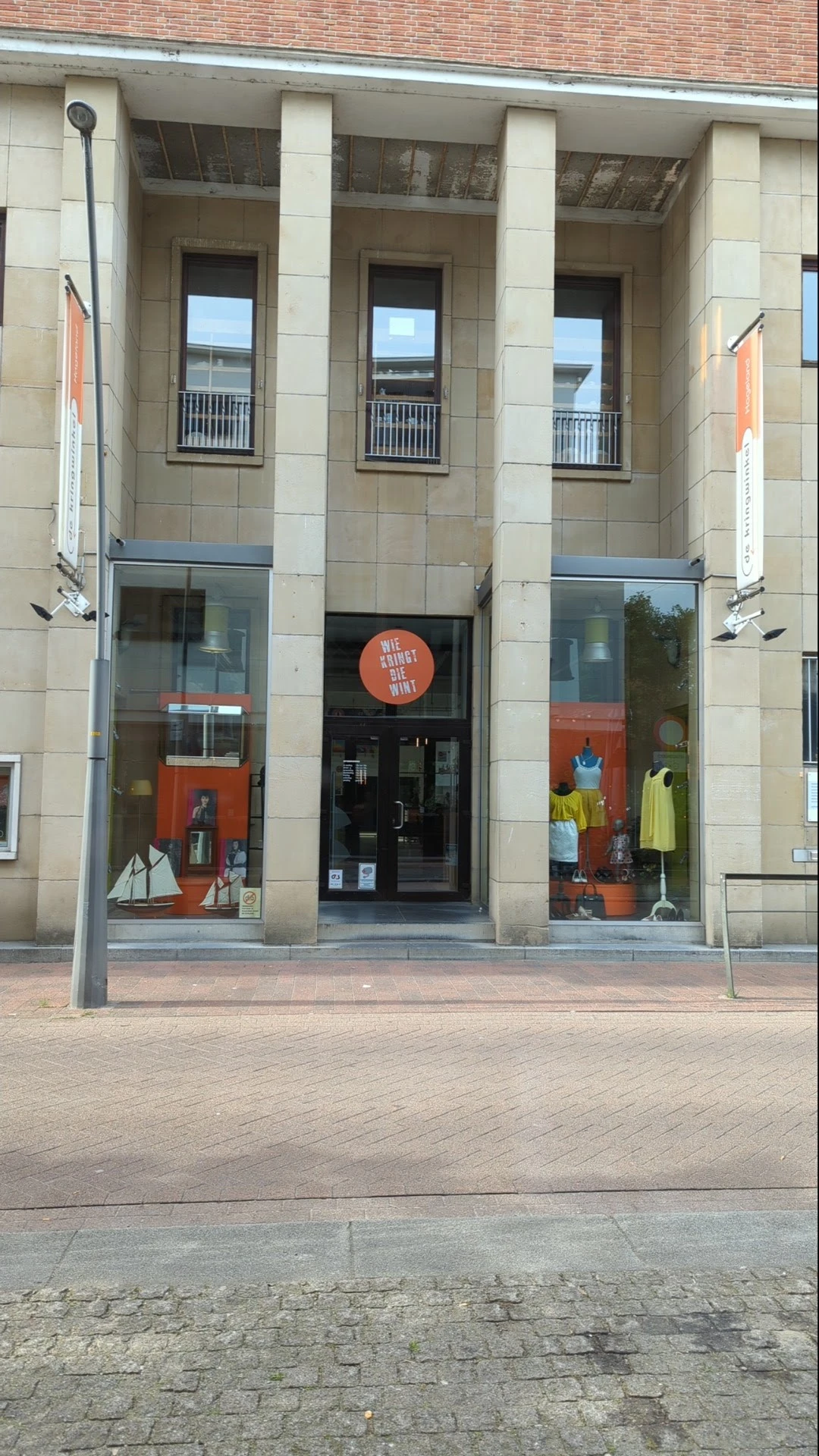 Winkelgevel met glazen deuren en ramen, oranje accenten in de vitrine en etalage met kleding