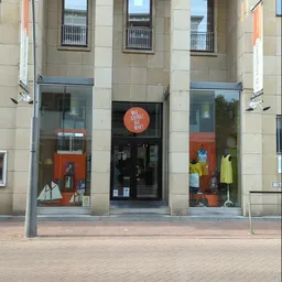 Winkelgevel met glazen deuren en ramen, oranje accenten in de vitrine en etalage met kleding