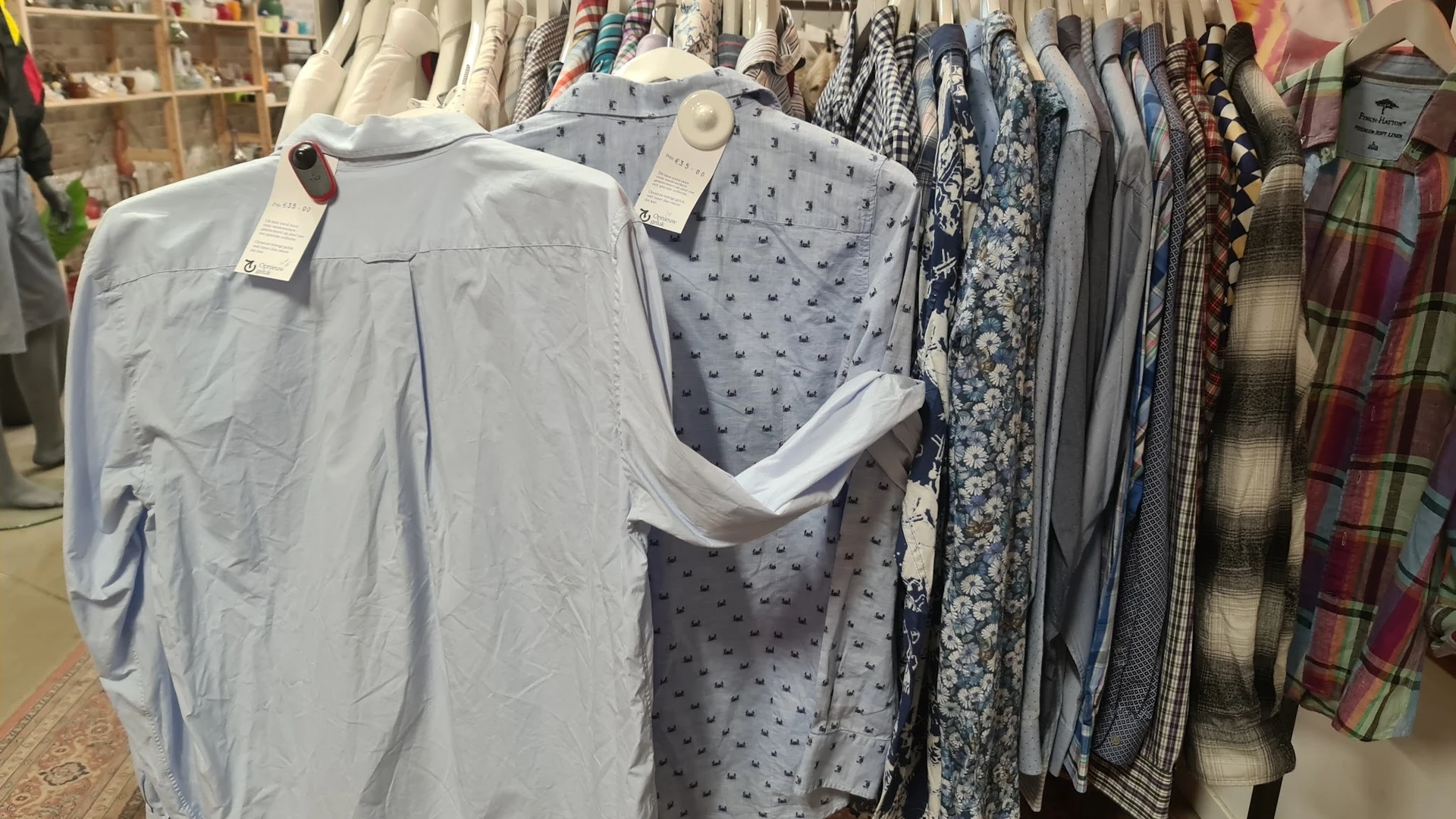 Rekken met tweedehands kleding, waaronder lichtblauwe en grijze items met patronen en effen kledingstukken op hangers