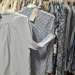 Rekken met tweedehands kleding, waaronder lichtblauwe en grijze items met patronen en effen kledingstukken op hangers