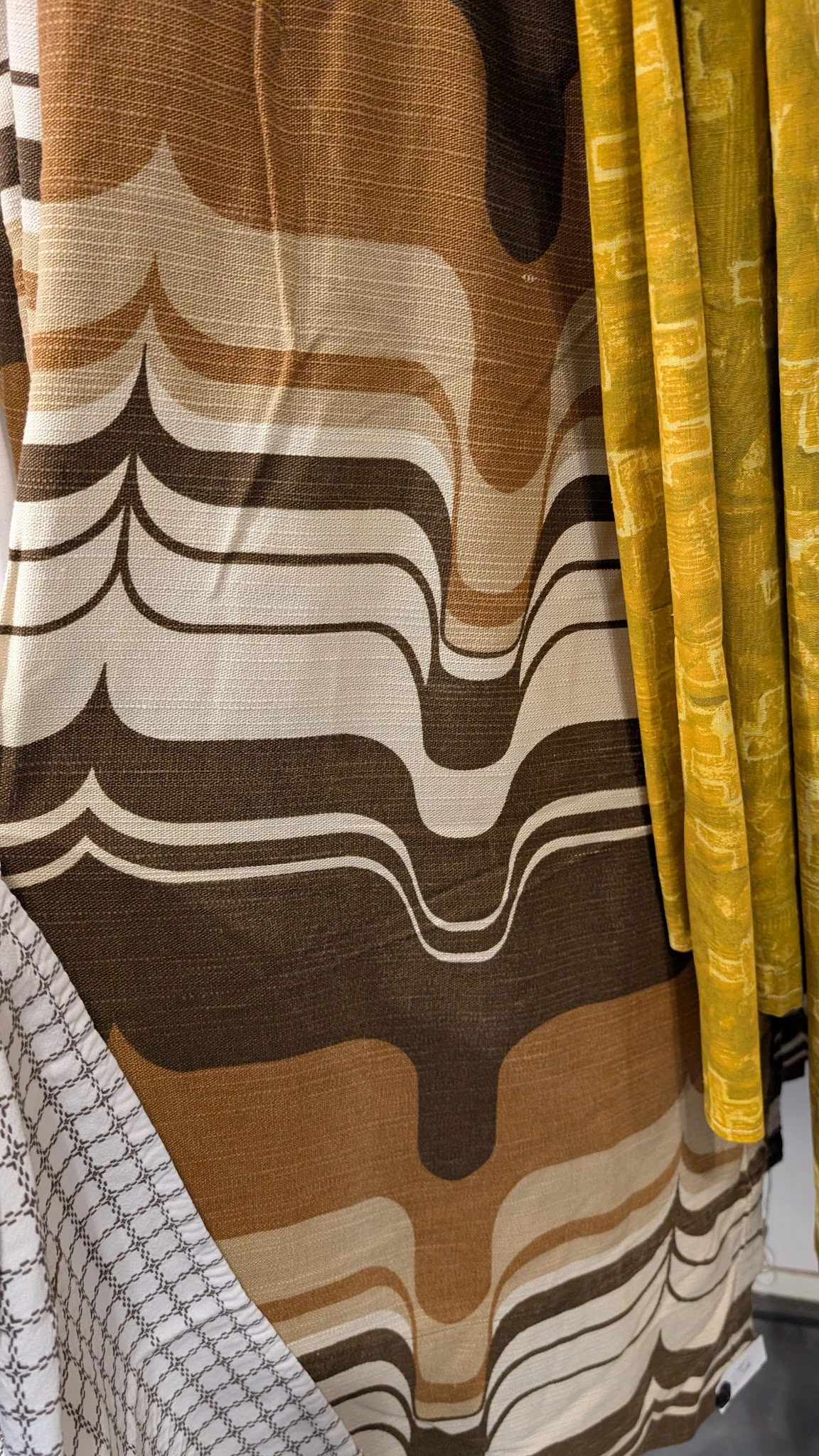 Golvend patroon op bruine en crème stoffen, mogelijk gordijnen of bekleding met gele gordijnen ernaast