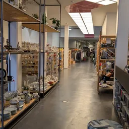 Winkelvloer van kringloopwinkel met stellingen, rekken met kleding en diverse spullen links en rechts