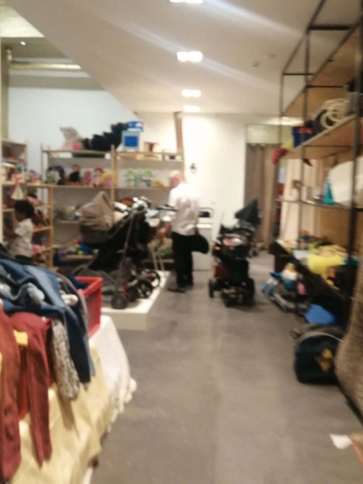 Rommelig winkelinterieur met stellingen, kleding, fietsen en diverse spullen verspreid over de vloer