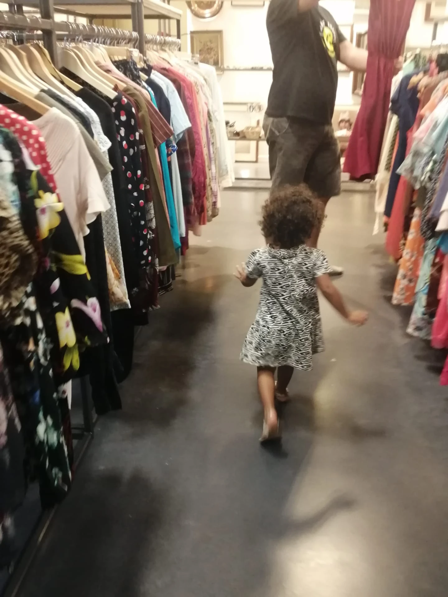 Kind loopt tussen kledingrekken in een winkelgang van de kringloopwinkel