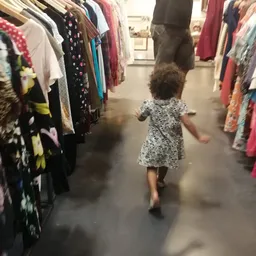 Kind loopt tussen kledingrekken in een winkelgang van de kringloopwinkel