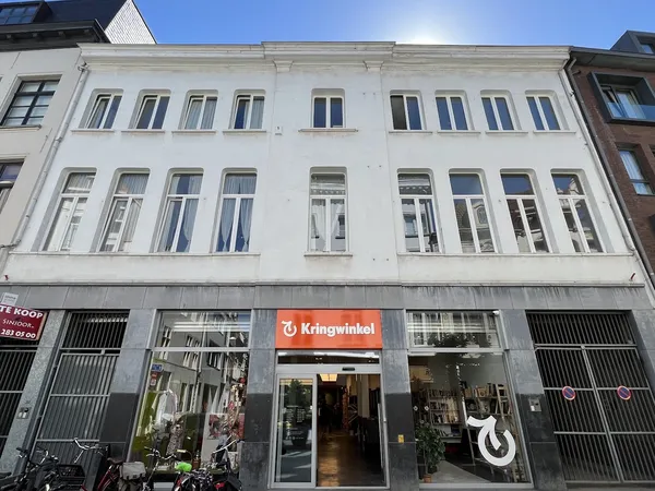 Witte gevel van een kringloopwinkel met rode Kringwinkel-logo op de begane grond en grote winkelramen