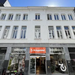Witte gevel van een kringloopwinkel met rode Kringwinkel-logo op de begane grond en grote winkelramen