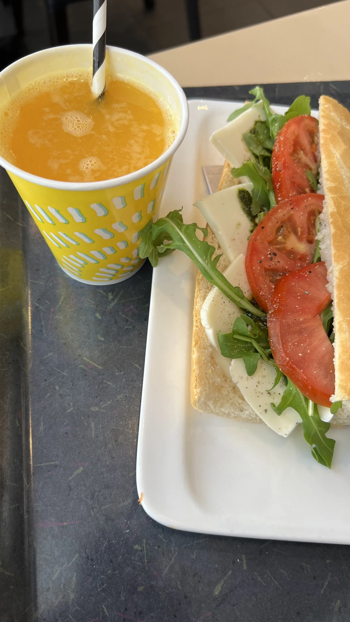 Broodje met tomaat, kaas en rucola op wit bordje naast geel kopje