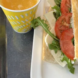 Broodje met tomaat, kaas en rucola op wit bordje naast geel kopje