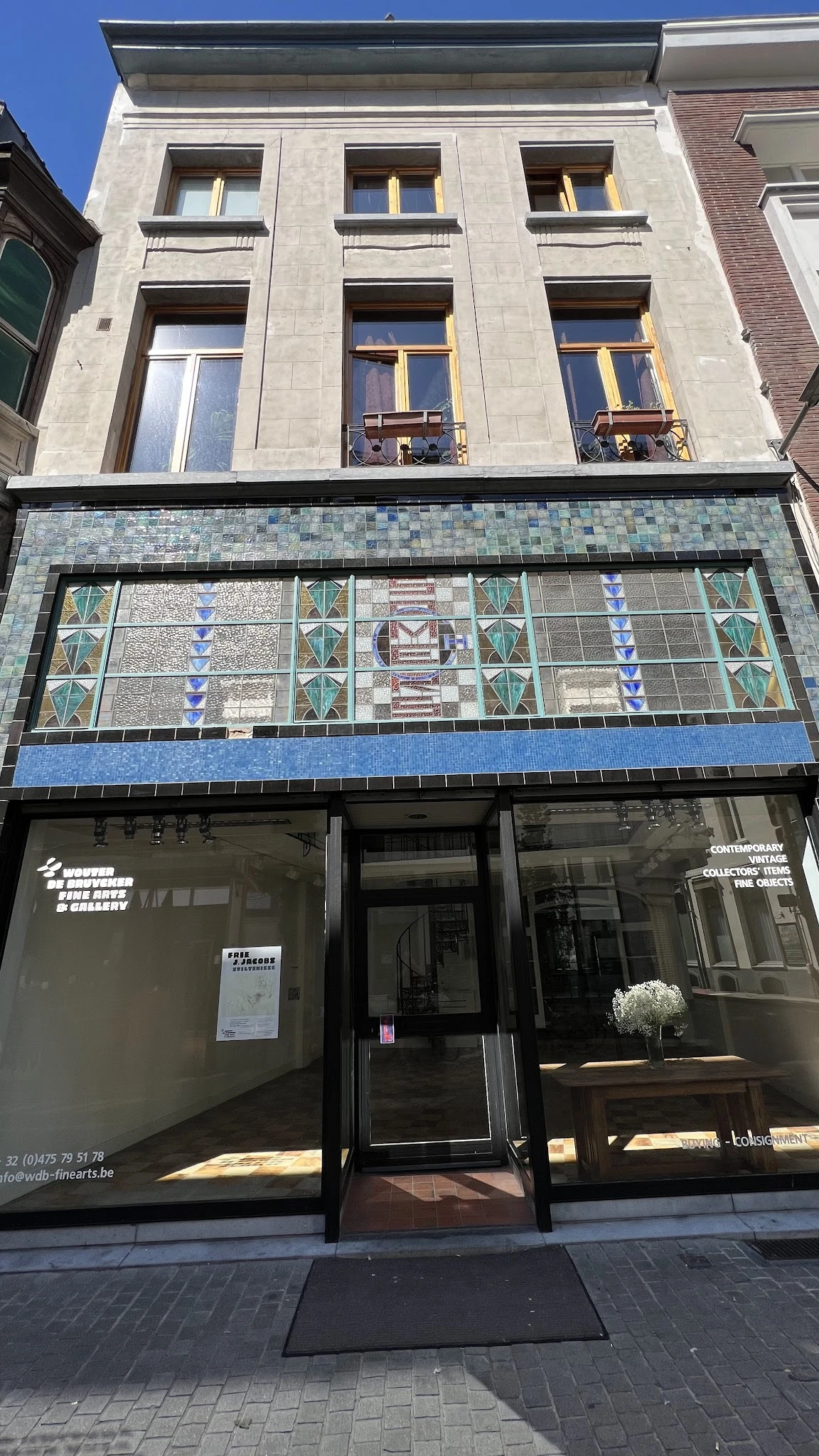 Gevel van kringloopwinkel met decoratieve tegelwerk in blauwe en groene tinten boven de ingang
