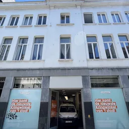 Witte gevel van kringloopwinkel met ramen op meerdere verdiepingen en grijze winkelgevel beneden met blauwe borden