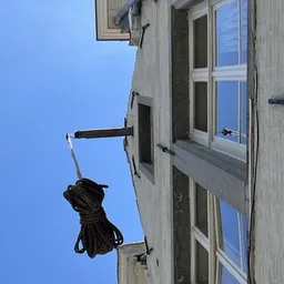 Schuin omhoog gefotografeerde gevel met raam en kraan tegen blauwe lucht