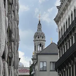 Uitzicht op een kerktoren met kruis tussen historische gebouwen in een stedelijke straat