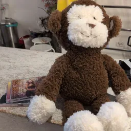 Bruine en witte pluchen aapknuffel op een tafel met een magazine ernaast